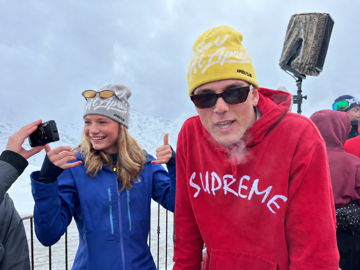 Yellow and grey Après Club beanies on a snowy mountain terrace