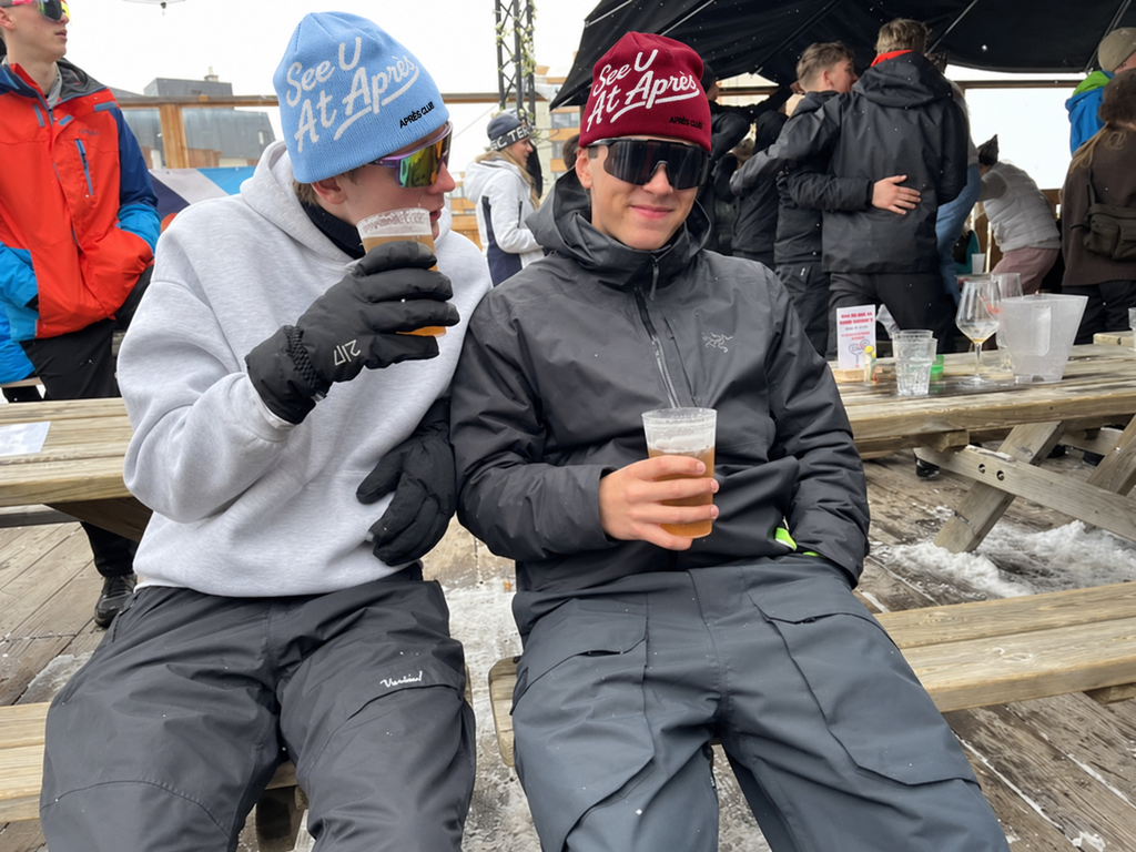 Baby blue and burgundy Après Club beanies on a terrace bench with a beer
